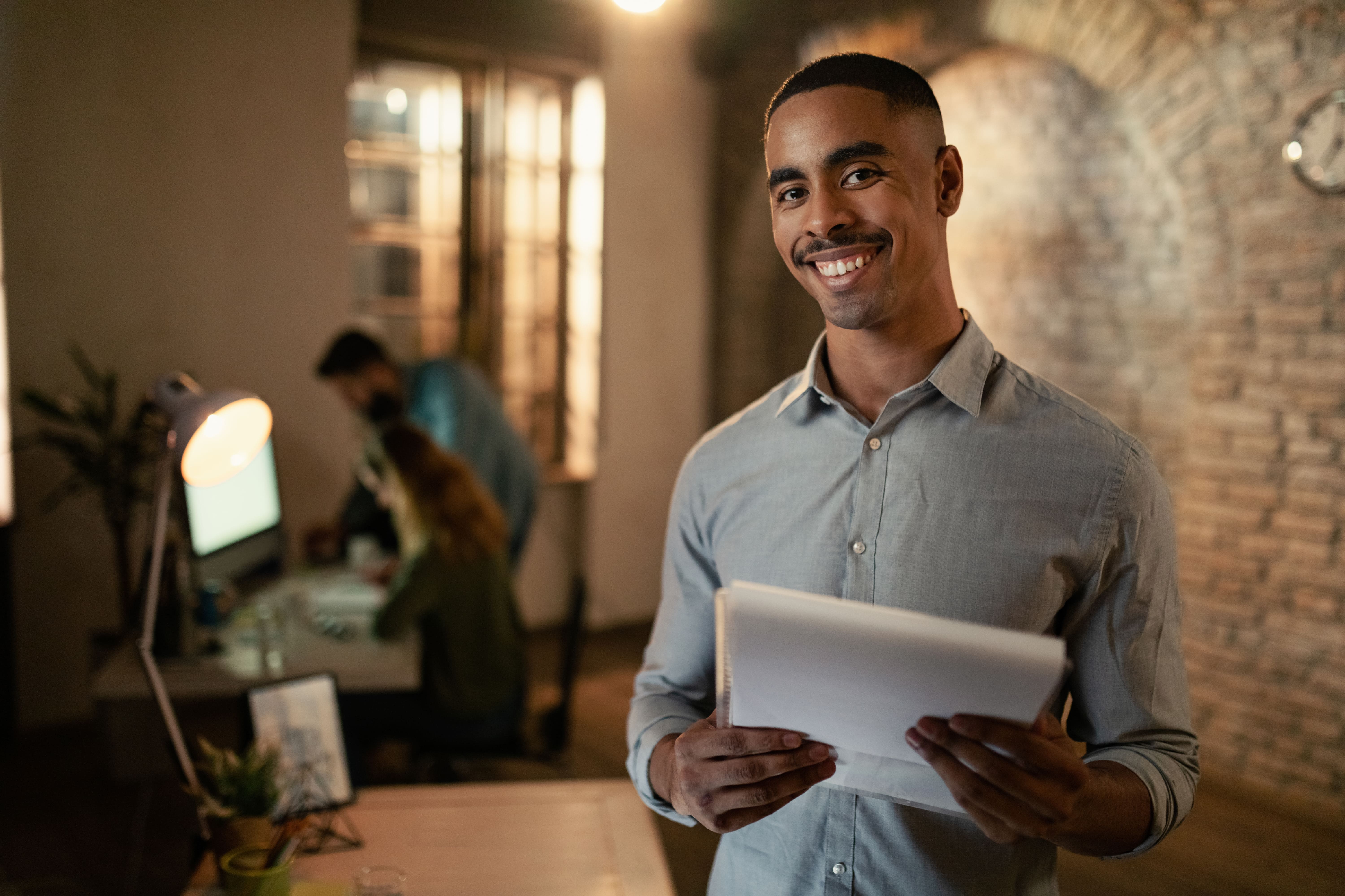 portrait-happy-black-entrepreneur-working-late-business-reports-looking-camera-office
